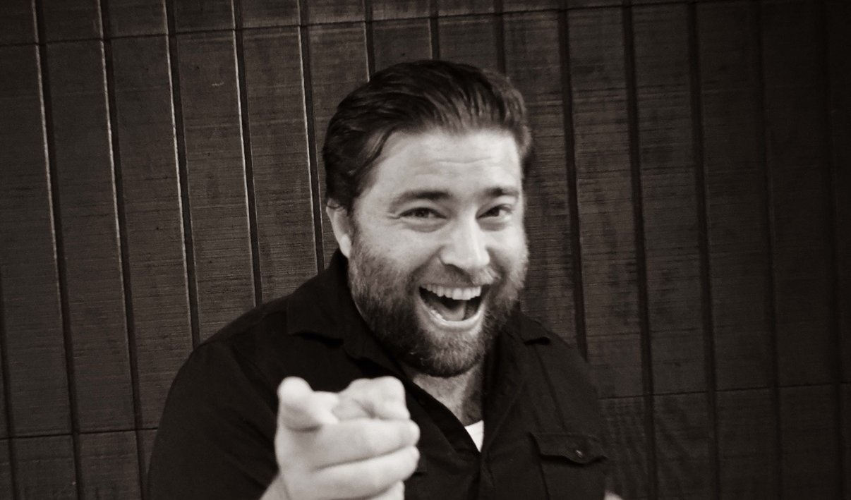 Black and white photo of Matt Long laughing and pointing at the camera